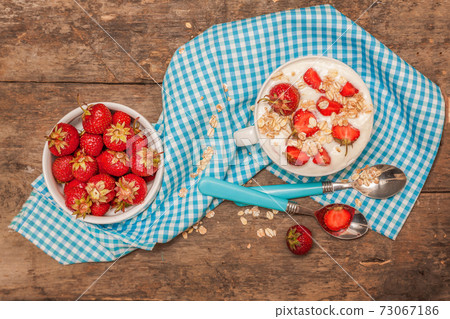In a cup of yogurt, oat granola and fresh strawberries, on a blu 73067186