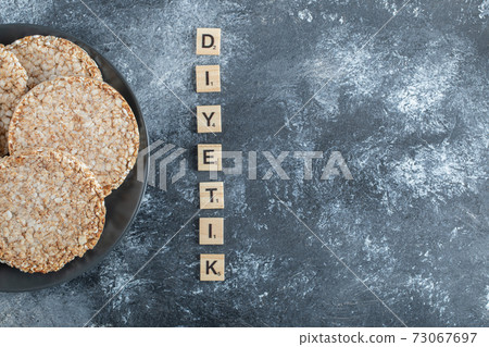 A black plate full of puffed rice bread on a marble background A black plate full of puffed rice bread on a marble background 73067697