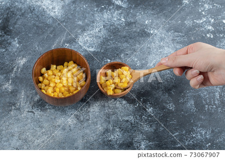 Hand holding a wooden spoon of popcorn seeds Hand holding a wooden spoon of popcorn seeds 73067907