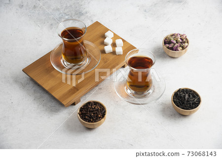 Glass cups of tea with sugar on a wooden board Glass cups of tea with sugar on a wooden board 73068143