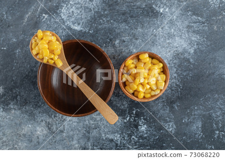 An empty wooden bowl with a wooden spoon of popcorn seeds 73068220