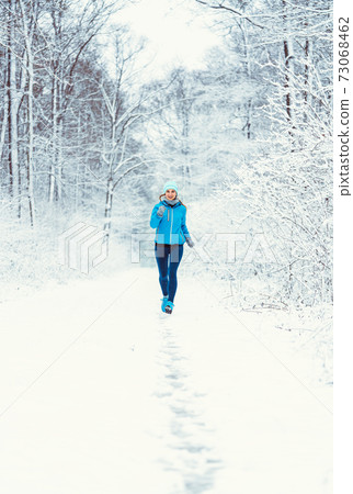 Woman jogging towards camera in cold and snowy forest Woman jogging towards camera in cold and snowy forest 73068462