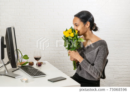 Young pretty mixed-raced woman holds a bunch of yellow roses in front of her face and speaking online Young pretty mixed-raced woman holds a bunch of yellow roses in front of her face and speaking online 73068596
