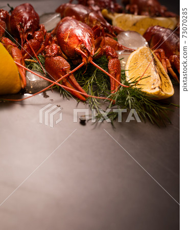 Boiled red crawfish, ready to eat with lemon slices and ice cubes on a black surface. 73070285