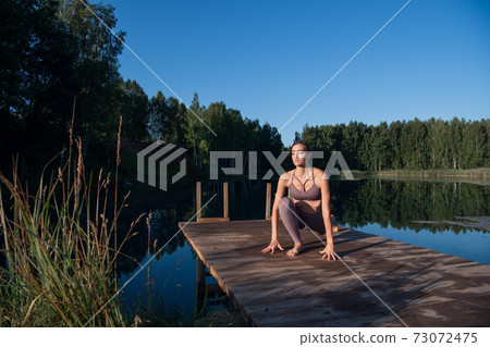 Healthy woman practicing yoga on the lake at sunrise enjoying positive energies from nature Healthy woman practicing yoga on the lake at sunrise enjoying positive energies from nature 73072475
