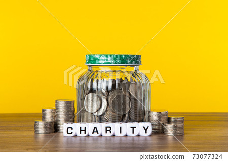 A lot coins in glass jar with yellow background. Saving for Charity concept 73077324