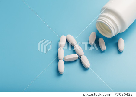 Vitamin A pills fell out of a white jar on a blue background. Vitamin A pills fell out of a white jar on a blue background. 73080422