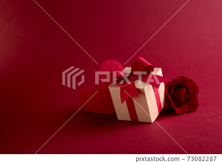 Happy st. Valentines day concept with craft paper gift box, red paper hearts and fresh rose against dark red background with space for text. Happy st. Valentines day concept with craft paper gift box, red paper hearts and fresh rose against dark red background with space for text. 73082287