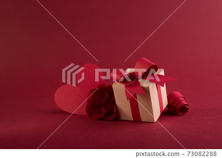 Happy st. Valentines day concept with craft paper gift box, red paper hearts and fresh rose against dark red background with space for text. Happy st. Valentines day concept with craft paper gift box, red paper hearts and fresh rose against dark red background with space for text. 73082288