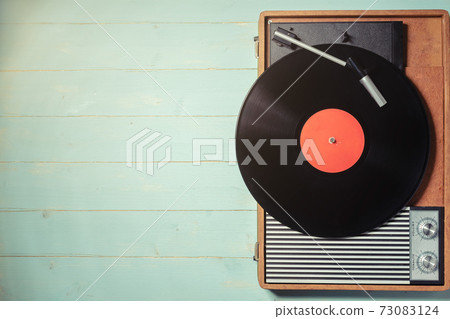 Old turntable with a vinyl record on green wooden table 73083124