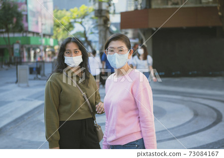 two asian woman wearing protection mask standing at bangkok city street 73084167