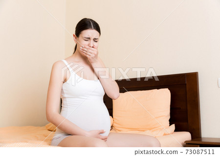 Pregnant suffering with nausea. Pregnancy symptoms, expectation toxicosis. Young vomiting woman sitting on bed. parenthood concept Pregnant suffering with nausea. Pregnancy symptoms, expectation toxicosis. Young vomiting woman sitting on bed. parenthood concept 73087511