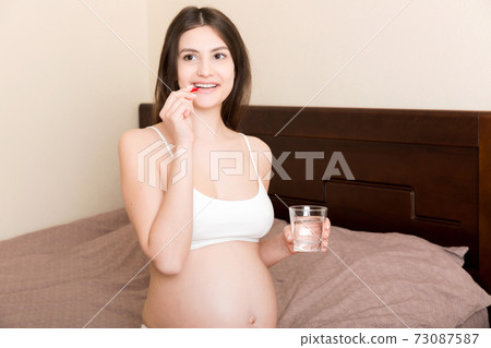 pregnant woman is sitting in sofa. Taking pills from colds. Last months of pregnancy 73087587