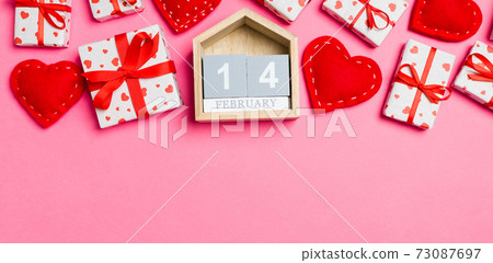 Top view of gift boxes, wooden calendar and red textile hearts on colorful background. The fourteenth of february. St Valentine's day concept with copy space 73087697