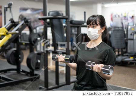 A woman wearing a mask and doing muscle training at a fitness gym 73087952