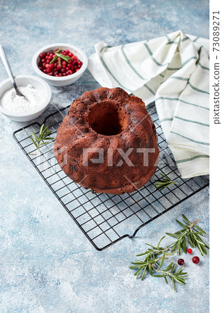 Chocolate bundt cake on a metal wire rack, powdered sugar and cranberries in bowls Chocolate bundt cake on a metal wire rack, powdered sugar and cranberries in bowls 73089271