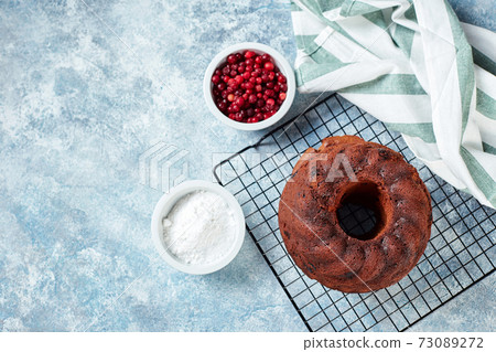 Chocolate bundt cake on a metal wire rack, powdered sugar and cranberries in bowls 73089272