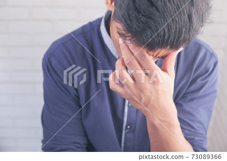 Young man suffering headache and covering his face with hand  73089366