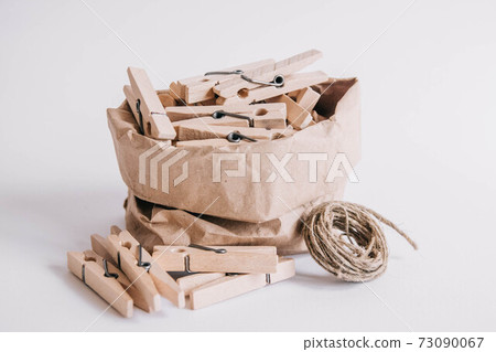 Wooden clothespins in paper bag with rope on white background. Place for your text 73090067
