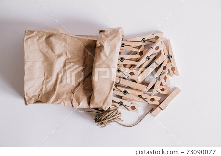 Wooden clothespins in paper bag with rope on white background. View from above. Place for your text 73090077