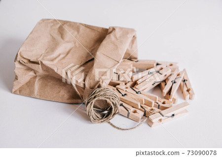Wooden clothespins in paper bag with rope on white background. View from above. Place for your text Wooden clothespins in paper bag with rope on white background. View from above. Place for your text 73090078