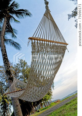 A relaxing rope hammock tied between two palm trees A relaxing rope hammock tied between two palm trees 73090171