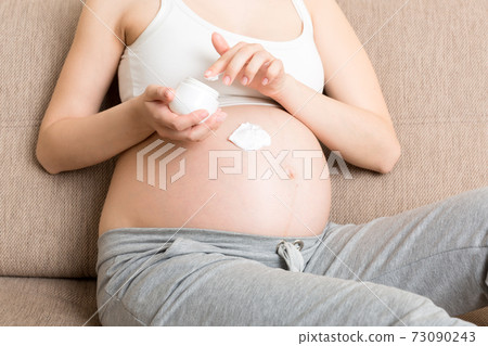 a pregnant girl sits at home on the bed and smears smile an anti-stretch mark cream on her stomach. Pregnancy, motherhood, preparation and expectation concept a pregnant girl sits at home on the bed and smears smile an anti-stretch mark cream on her stomach. Pregnancy, motherhood, preparation and expectation concept 73090243