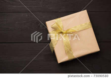 box wrapped in brown paper and tied with a golden ribbon with a bow, gift on a wooden background box wrapped in brown paper and tied with a golden ribbon with a bow, gift on a wooden background 73090580