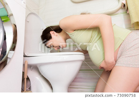 Sick young woman with pain in stomach is vomiting in toilet sitting on the floor at home. Young woman vomiting into the toilet bowl in bathroom Sick young woman with pain in stomach is vomiting in toilet sitting on the floor at home. Young woman vomiting into the toilet bowl in bathroom 73090758