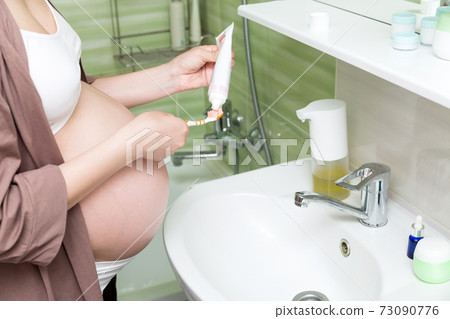 Young pregnant woman dressed in a robe in the bathroom at home. Cute adult girl in the third trimester of pregnancy in the home bathroom brushing her teeth Young pregnant woman dressed in a robe in the bathroom at home. Cute adult girl in the third trimester of pregnancy in the home bathroom brushing her teeth 73090776