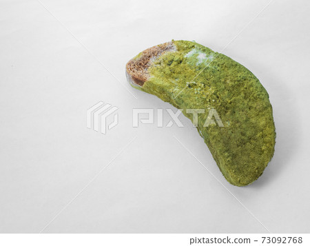 A piece of bread covered with green mold on a white background isolate 73092768