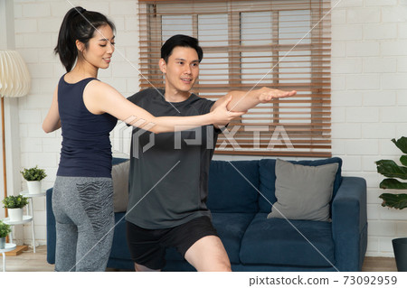Healthy young Asian couple exercises in home and wife teaching her husband for exercise in COVID-19 quarantine at home. A new normal lifestyle and healthy exercise can be done anywhere. Healthy young Asian couple exercises in home and wife teaching her husband for exercise in COVID-19 quarantine at home. A new normal lifestyle and healthy exercise can be done anywhere. 73092959