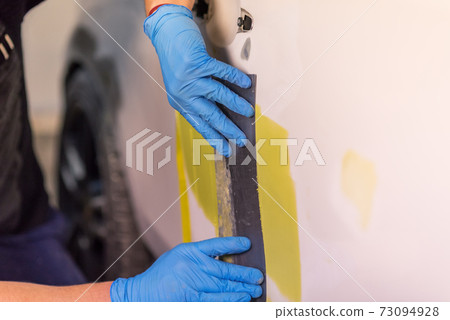 Repairing car body, Application putty close up. The mechanic repair the car. Work after the accident by working sanding primer before painting. 73094928