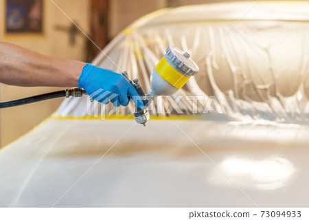 Man with protective clothes and mask painting car using spray compressor. Selective focus. Man with protective clothes and mask painting car using spray compressor. Selective focus. 73094933