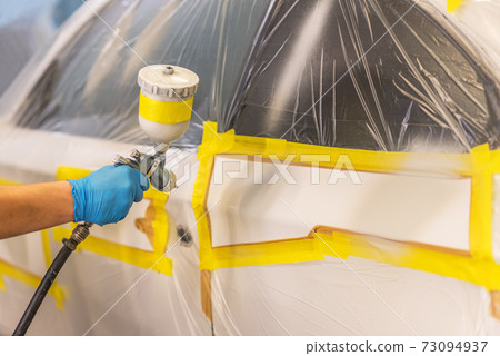 Man with protective clothes and mask painting car using spray compressor. Selective focus. 73094937