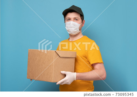 Delivery man holding cardboard box in medical rubber gloves and mask 73095345