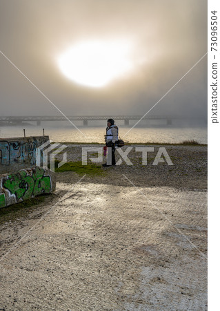 A winter picture of a woman with a fishing rod. Blue ocean and mist in the background. Picture from Malmo, southern Sweden A winter picture of a woman with a fishing rod. Blue ocean and mist in the background. Picture from Malmo, southern Sweden 73096504