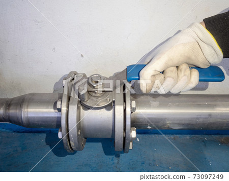 Hand with safety glove opened ball valve on silver stainless pipe 73097249