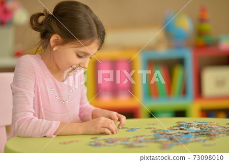 Portrait of cute little girl collecting puzzle pieces 73098010