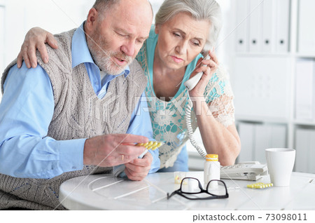 Portrait of ill Senior couple at home calling doctor Portrait of ill Senior couple at home calling doctor 73098011
