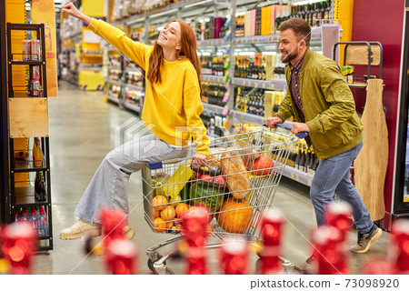 side view on man pushing shopping cart with redhedad woman sitting in it 73098920