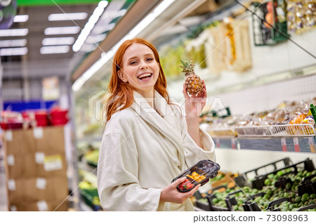 happy caucasian woman with red hair buying fresh vegetables and fruits in supermarket 73098963