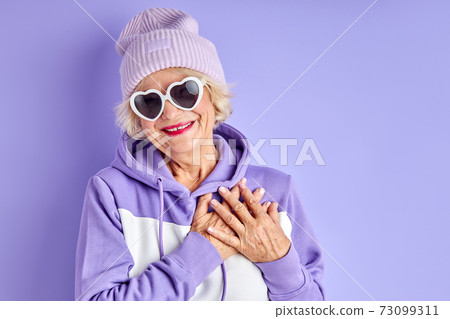 happy positive elderly woman holding hands on chest smiles happy positive elderly woman holding hands on chest smiles 73099311