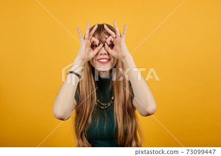 Making glasses fingers, looking at camera, smiling, funny, hold hands near eyes Making glasses fingers, looking at camera, smiling, funny, hold hands near eyes 73099447