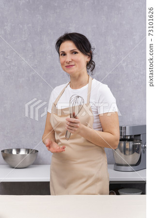 Woman cook in kitchen apron and with whisk in her hands. Vertical frame 73101626