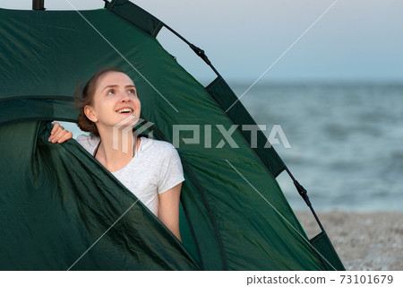 Happy woman sits in tent against the sea backdrop. Camping on the beach. Traveling and active lifestyle concept. Happy woman sits in tent against the sea backdrop. Camping on the beach. Traveling and active lifestyle concept. 73101679