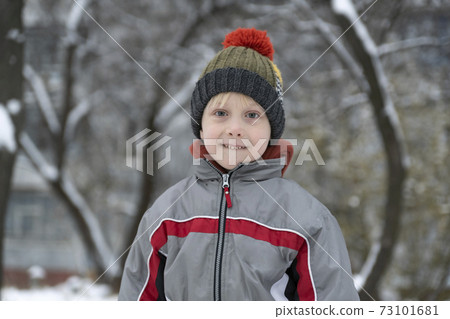 Portrait of child in winter hat against snowy yard background. Portrait of child in winter hat against snowy yard background. 73101681