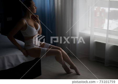 Seductive woman in lingerie sitting on bed 73101759