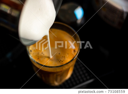 Close focus on pouring steam milk into shot of hot espresso coffee on glass cup. 73108559