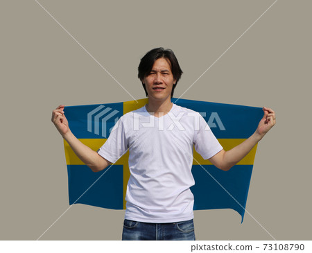 The man holding Sweden flag on his shoulder on grey background. 73108790